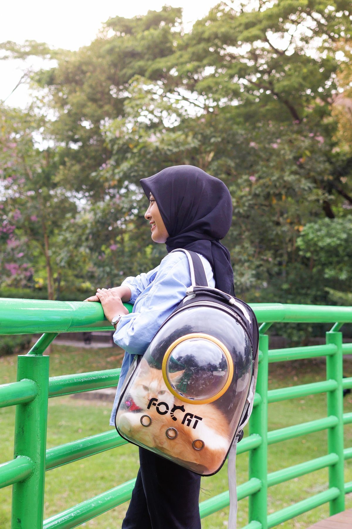 Woman with a cat carrier backpack on a bridge.